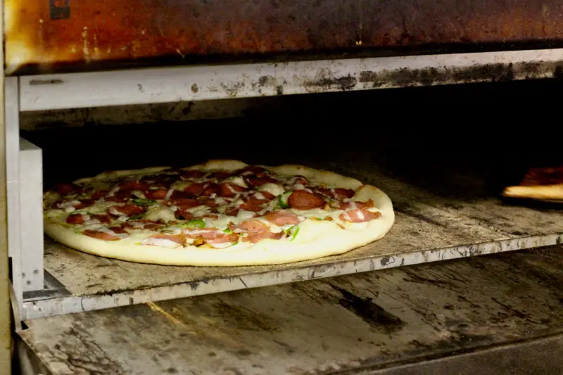 A pepperoni and pepper pizza baking on the stone deck of the Little Oven Pizza oven
